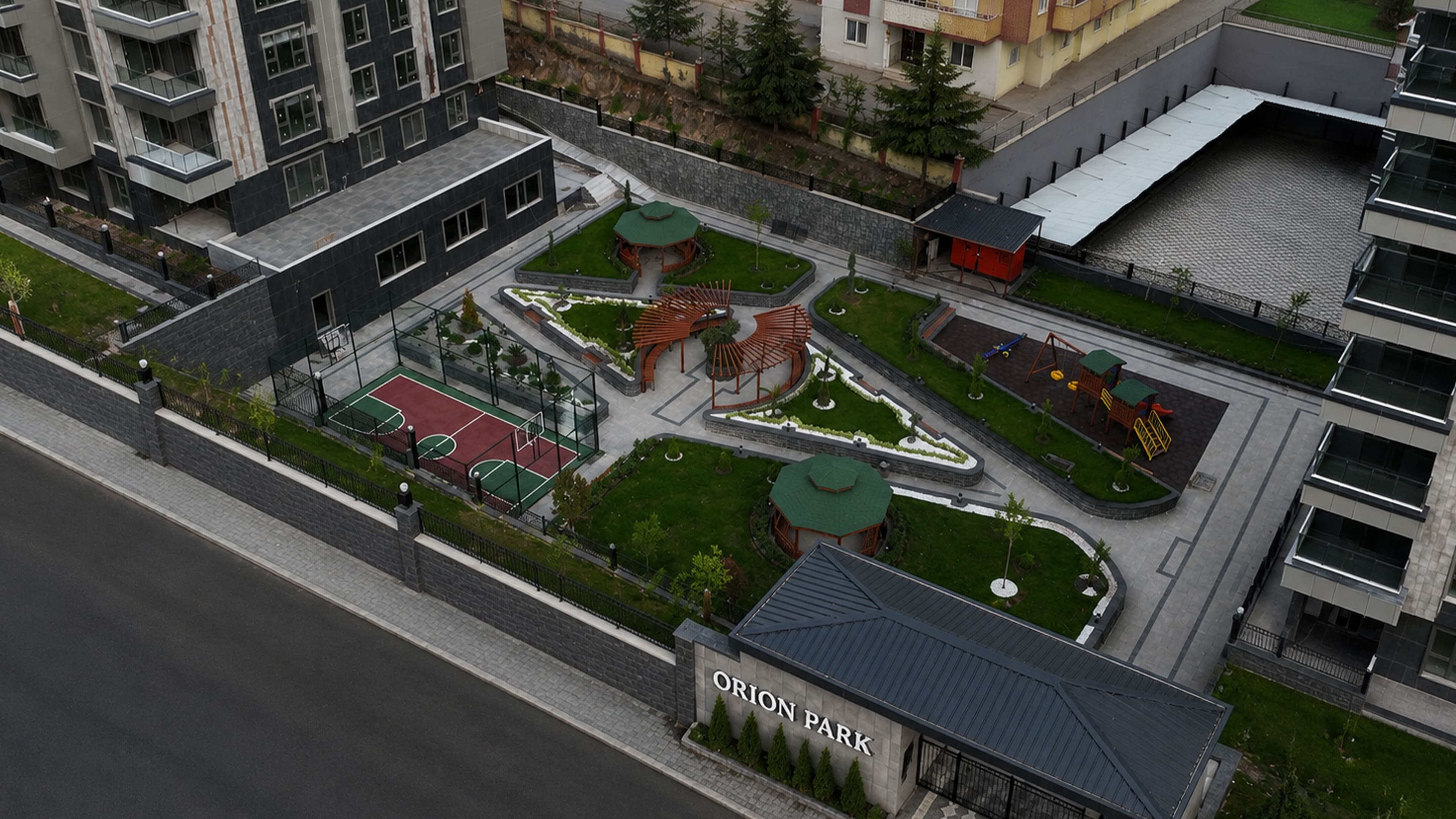 Orion Park'ın havadan görünümü; blokların solunda çiçekli yeşil park, avlusunda çocuk oyun alanı ve düzenlenmiş peyzaj