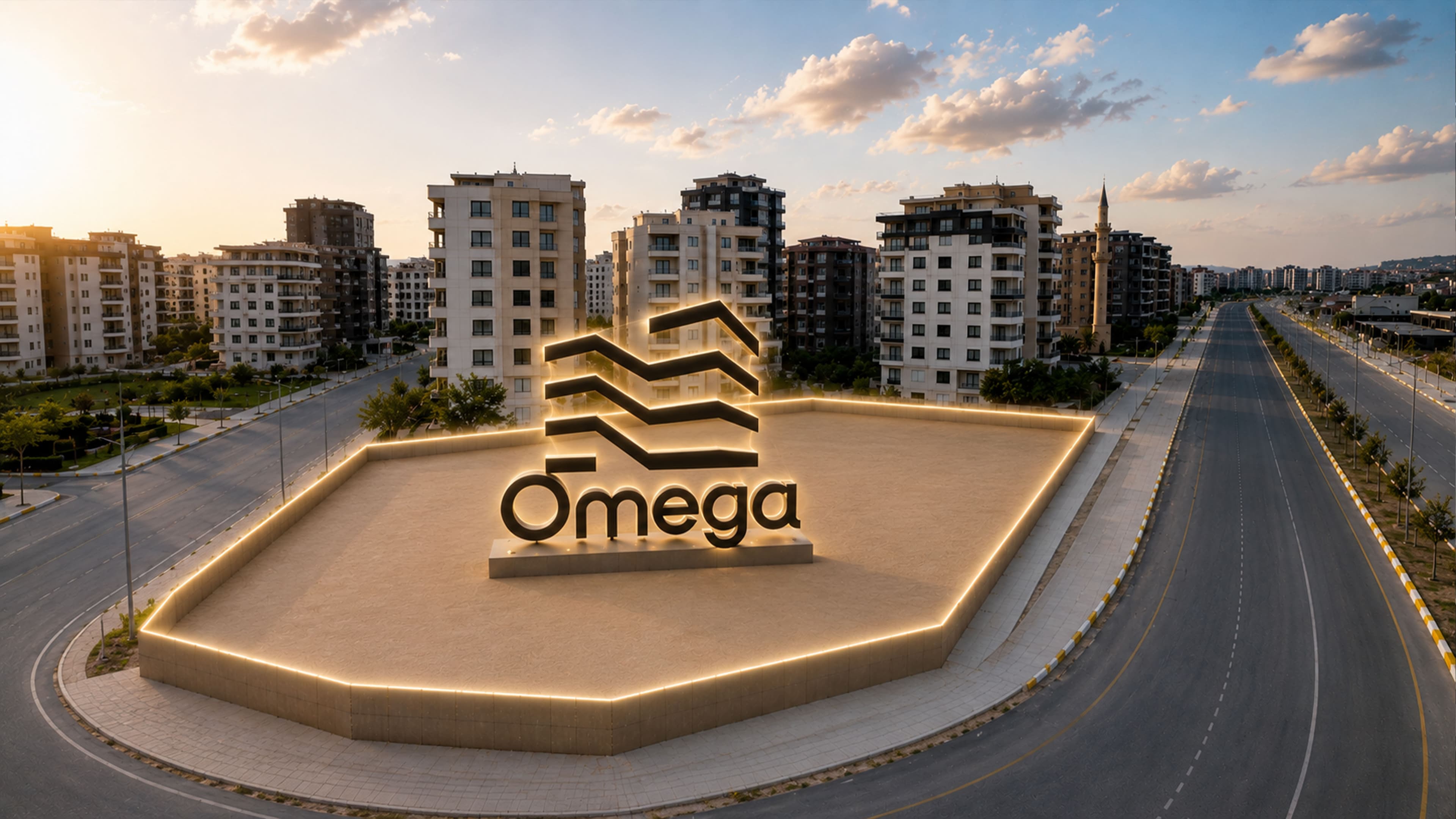 Buluntu Hoca Bulvarı kavşağındaki Omega anıt tabelası, gün batımında ışıklandırılmış peyzaj adasında; arkasında konut blokları ve ağaçlandırılmış bulvar