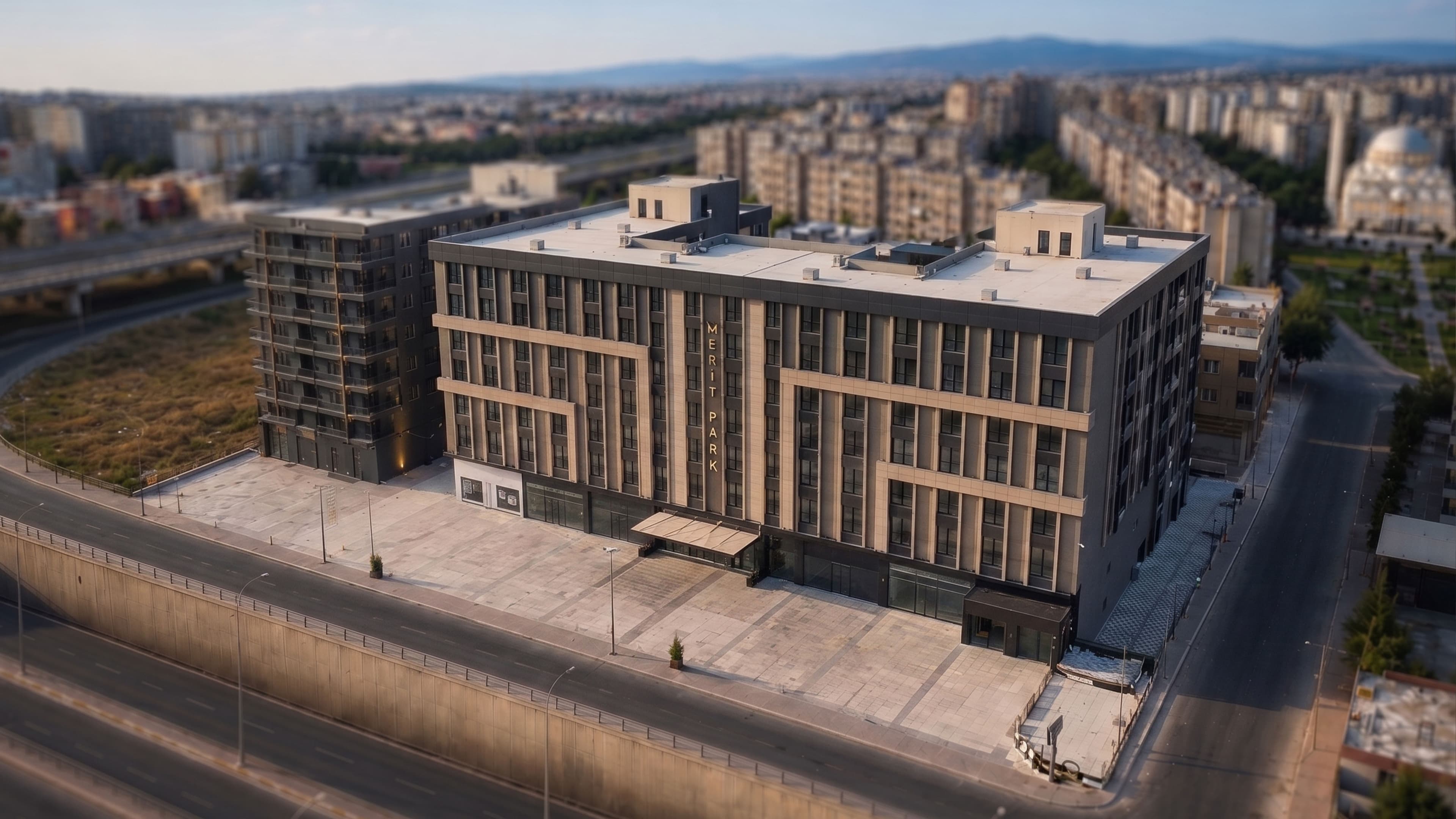 Şanlıurfa'nın havadan geniş görünümü; önde Merit Park'ın antrasit cepheli bloğu, solda viyadük, sağda kubbeli cami ve ufka uzanan şehir dokusu
